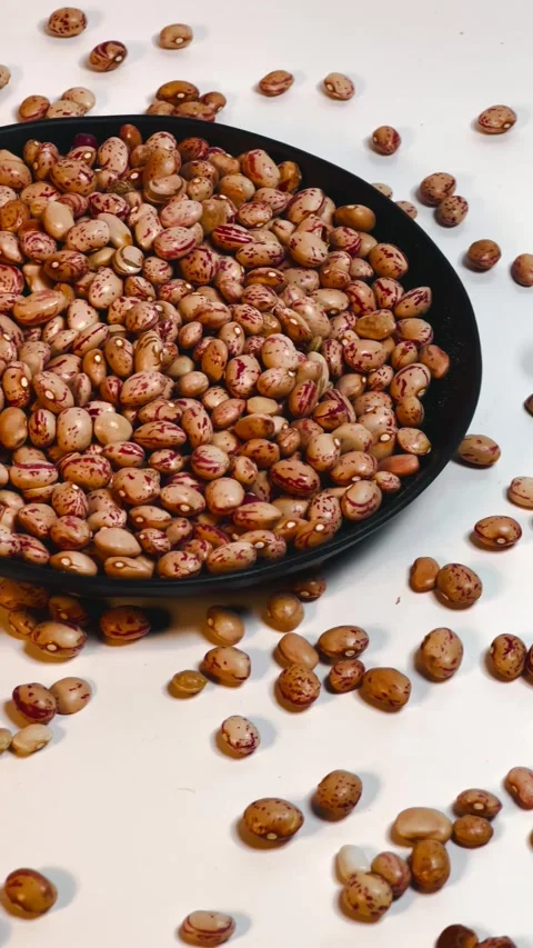 Raw pinto beans in dark plate, white background, vertical format, angled view Stock Footage 336471836