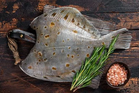Raw plaice flatfish fish on butcher board with knife. Dark wooden background Stock Photos