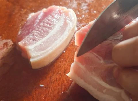 Raw Pork Being Cut with a Kitchen Knife on a Wooden Cutting Board Stock-Fotos