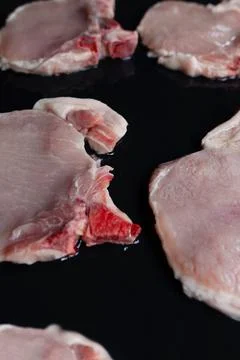Raw pork chops on black baking tray seasoned with oil and ready for barbecue Stock Photos