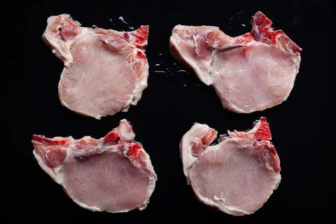 Raw pork chops on black baking tray seasoned with oil and ready for barbecue Stock Photos
