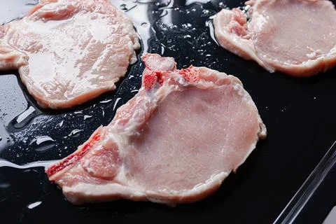Raw pork chops on black baking tray seasoned with oil Foto stock
