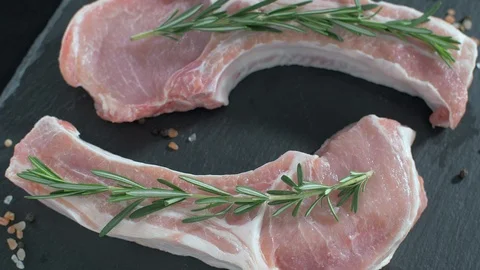 Raw pork chops with bone. Rosemary falls on raw meat. Video stock 106472484