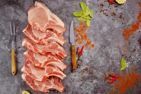 Raw pork chops bone in with spices on dark background. Stock Photos