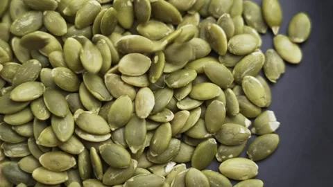 Raw pumpkin seeds falling onto a dark platter Stock Footage 337413505