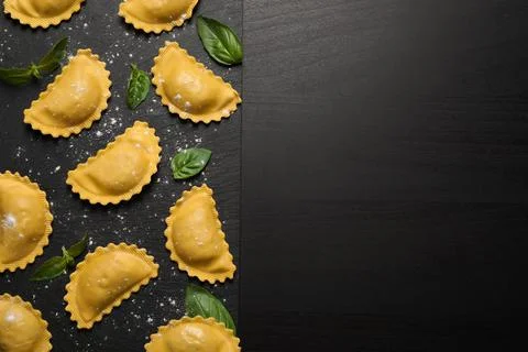Raw ravioli with basil on black table, flat lay and space for text. Italian p Stock Photos