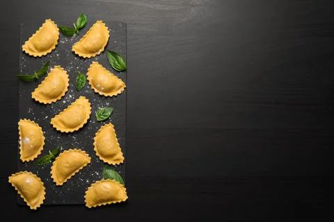 Raw ravioli with basil on black table, flat lay and space for text. Italian p Stock Photos