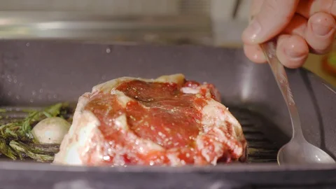 A raw red beef steak roasting on a black hot grill pan and pouring oil on it by Stock Footage 104434593