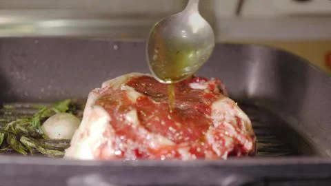 A raw red beef steak roasting on a black hot grill pan and pouring oil on it by Stock Photos