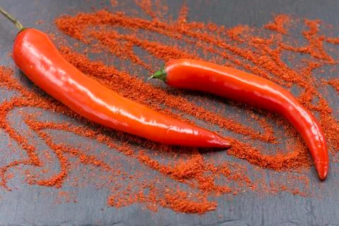 Raw red chili peppers and ground paprika on dark slate plate. Stock Photos