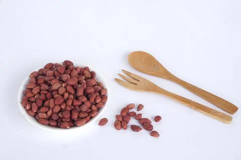 Raw red-skinned peanuts in a white bowl with bamboo spoon and fork on a white ba Fotos Stock