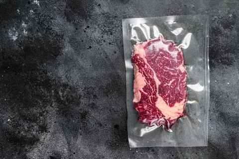 Raw rib eye beef meat steak in vacuum packaging. Black background. Top view Stock Photos