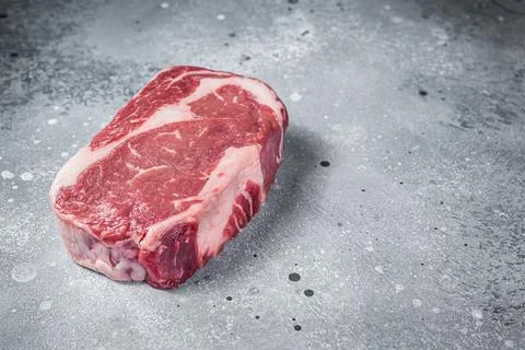Raw Rib Eye Steak, beef marbled meat on butcher board. Gray background. Top view Stock Photos