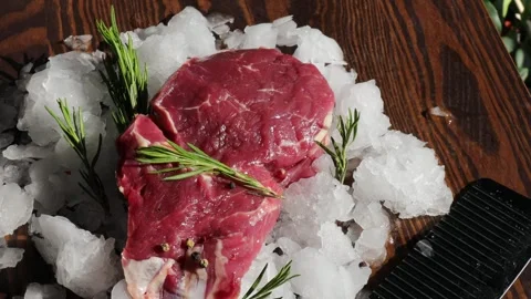 Raw Ribeye Beef Steak on Crushed Ice with Rosemary on Wooden Background, Fresh Stock Footage 310337740