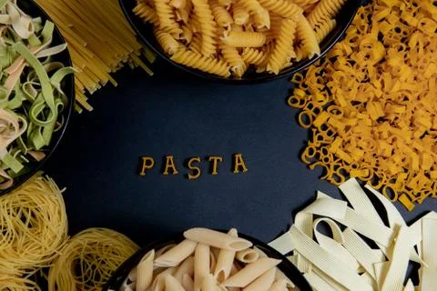 Raw round pasta on a dark background. The word PASTA made of wooden letters i Foto stock