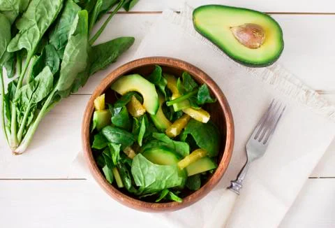 Raw salad of spinach, avocado and orange in wooden plate on white background Stock Photos
