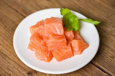 Raw salmon filet cube with herbs and spices on white plate on wooden backgrou Stock Photos