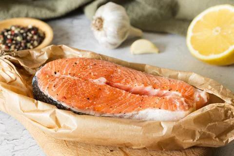 Raw salmon fish steak on in baking paper, lemon, peppers Stock Photos