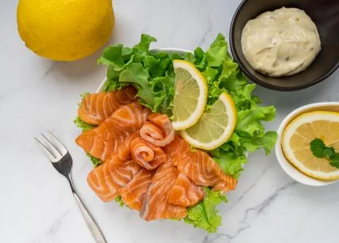 Raw salmon slice or salmon sashimi with green oak salad, lemon and white sauc Stock Photos