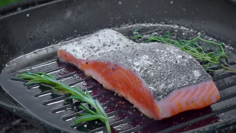 Raw salmon steak is being cooked on a hot cast iron pan with rosemary and thyme. Stock Footage 317931657