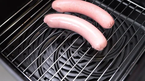Raw sausages being placed one by one on an air fryer rack for cooking Stock-Footage 347632290