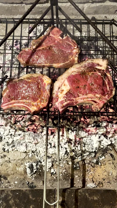 Raw seasoned T-bone steaks on wire grid grilled over hot coals Vídeo Stock 337799250