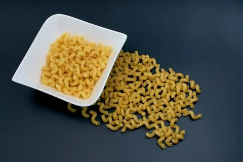 Raw small pasta in the shape of a spring. Pasta in a white plate on a dark fo Stock Photos