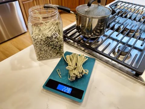 Raw spaghetti on scale next to container with stainless steel pot on top of.. Stock Photos