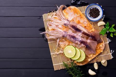Raw squid on ice with lemon garlic spice salad on black wooden table backgr.. Foto stock