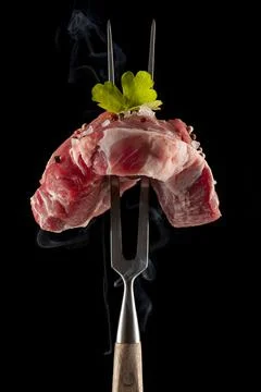 Raw steak on a big meat fork on black background Stock Photos
