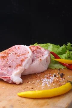 Raw steak, chop on a rustic cutting board with salt, pepper and grinder for Stock Photos