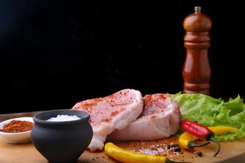 Raw steak, chop on a rustic cutting board with salt, pepper and grinder for Stock Photos