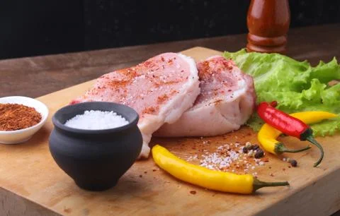 Raw steak, chop on a rustic cutting board with salt, pepper and grinder for s Foto stock