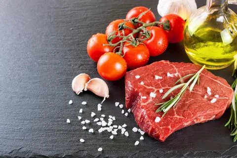 Raw steak with cooking ingridients on black slate background Stock Photos