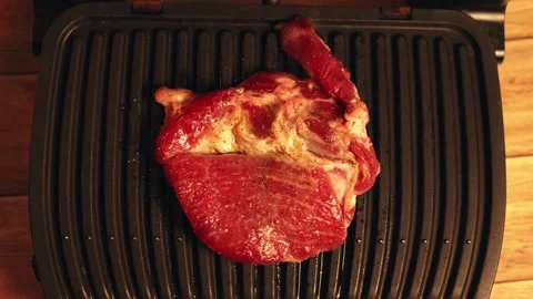 Raw steak cooking on a ribbed electric grill with wooden background Stock Footage 340562742