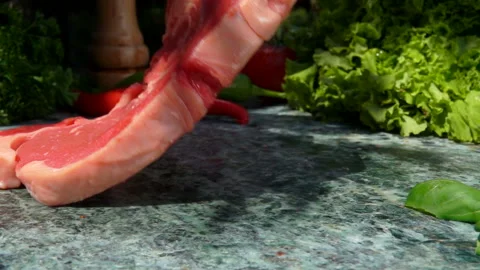 Raw steak is falling on a stone table on the background of fresh vegetables Stock Footage 129388445