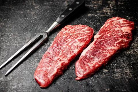 Raw steak with fork on the table. Stock Photos