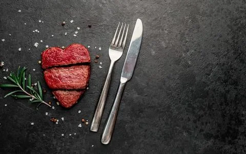 Raw steak meat with fork and knife on dark surface Stock-Fotos