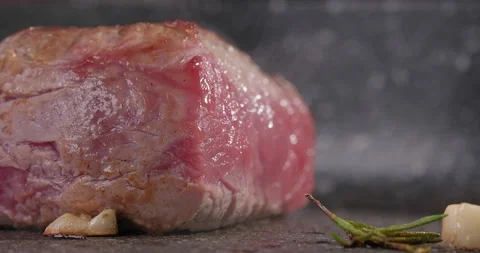 Raw steak roasting with rosemary and garlic on a frying pan. Steam rising above Stock Footage 261746902