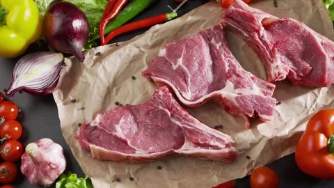 Raw steaks lie on a professional kitchen table with various vegetables. Fresh Stock Footage 240170721