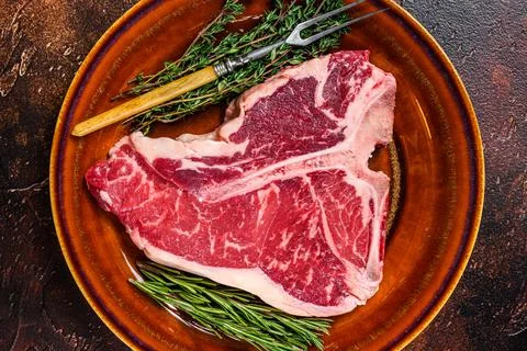 Raw T-bone beef meat Steak with herbs on a plate. Dark background. Top view Stock Photos