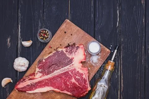 Raw T-bone beef steak on the wooden board and spices on black table. Stock Photos