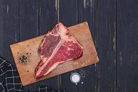 Raw T-bone beef steak on the wooden board and spices on black table. Stock Photos