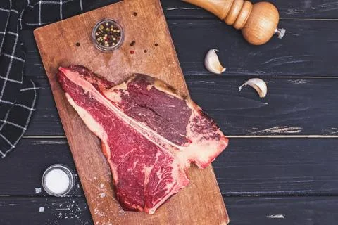 Raw T-bone beef steak on the wooden board and spices on black table. Stock Photos