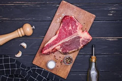 Raw T-bone beef steak on the wooden board and spices on black table. Stock Photos
