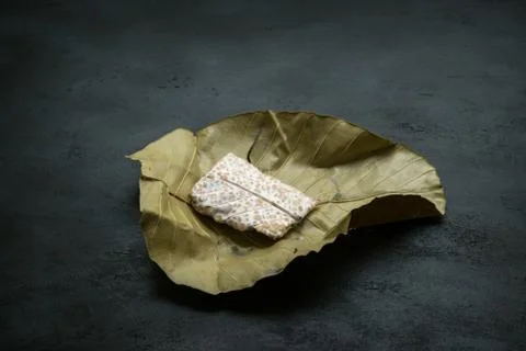 Raw tempeh wrapped in leaf, dark background. Stock Photos