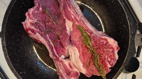 Raw tomahawk beef steaks sizzling in hot skillet pan with fresh rosemary an.. Stock Footage 339386985