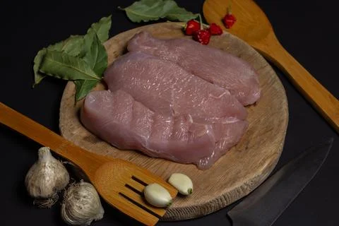 Raw turkey steaks on a black background. Turkey breast fillet on a wooden board. Stock Photos