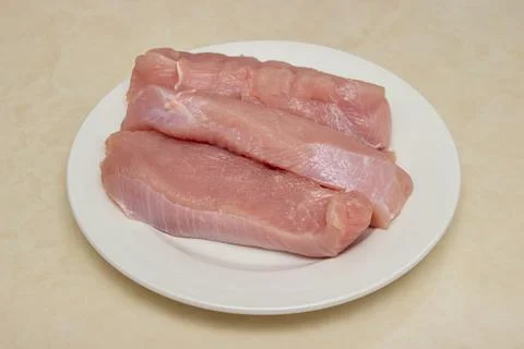 Raw turkey steaks on the kitchen table. Turkey breast fillet on a plate. Stock Photos