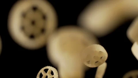 Raw wagon wheels pasta flies against black background after being exploded Stock Footage 88700928